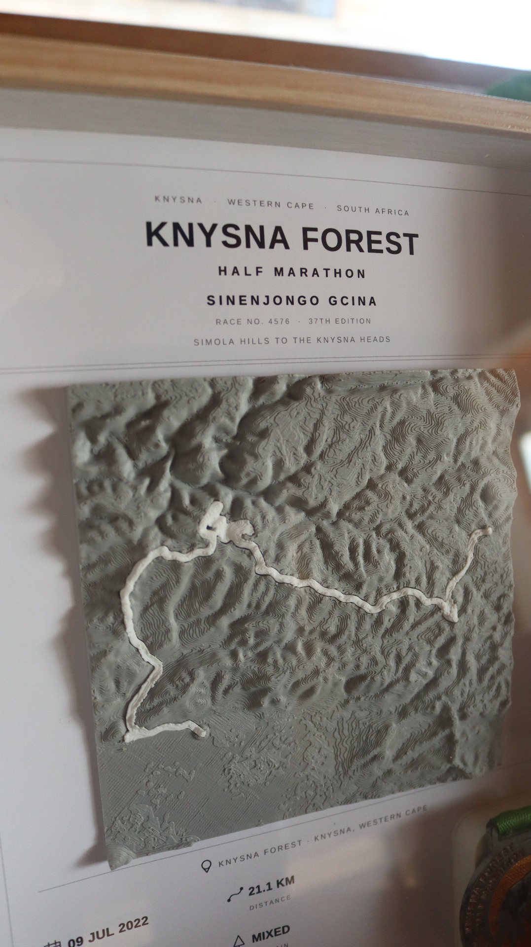 Close-up of a framed race display showing the printed 3D texture of the terrain and the raised white route line