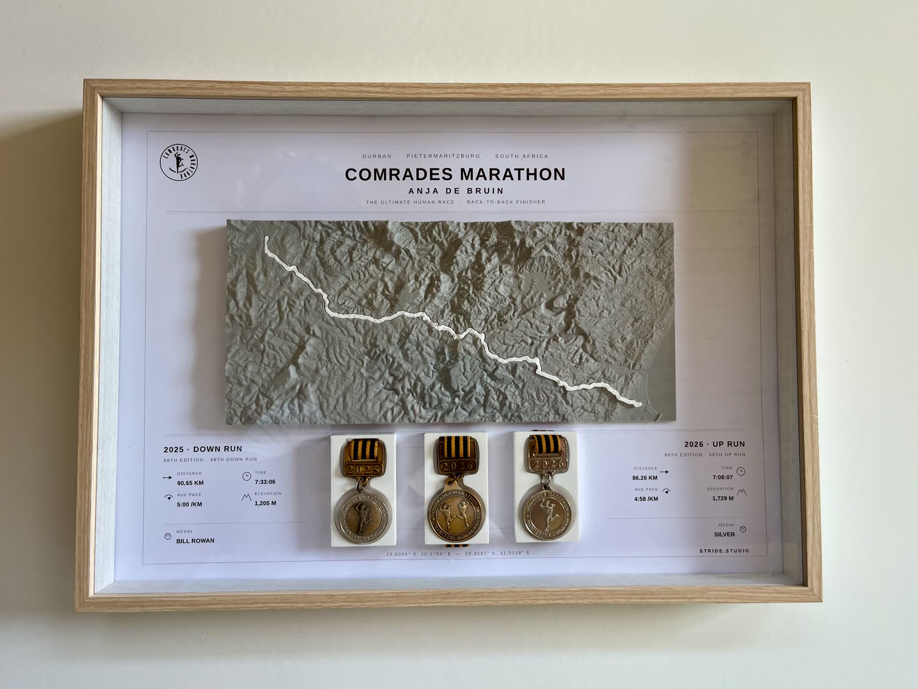 Comrades Marathon back-to-back finisher display with three medals and a 3D route relief in an oak frame